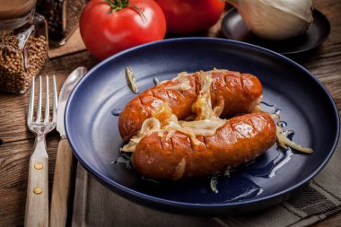 Kızarmış sosis bir tabak içinde soğan ile.