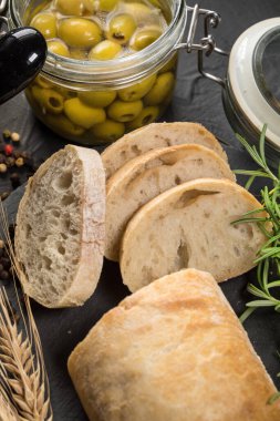 İtalyan ciabatta ekmeği. Koyu arkaplanda taş kesme tahtasına dilimlenmiş..