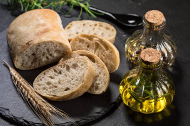 İtalyan ciabatta ekmeği. Koyu arkaplanda taş kesme tahtasına dilimlenmiş..