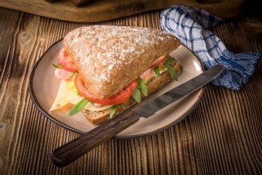 Tahta bir masada peynirli, jambonlu ve domatesli üçlü sandviç..