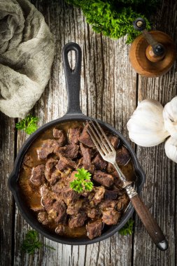 Dökme demir tavada sığır güveci, ahşap arka plan. Yüzeyin derinliği. Üst görünüm.