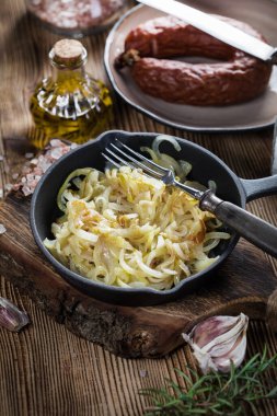 Tahta bir tezgahta duran dökme demir bir tavada kızarmış soğan..