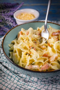 Tagliatelle Carbonara 'yı ahşap masada kasede yosunluyor. Sığ alan derinliği.