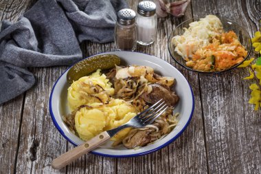 Kızarmış ciğer, soğan ve elma haşlanmış patates ve salatalık turşusuyla servis edilir..