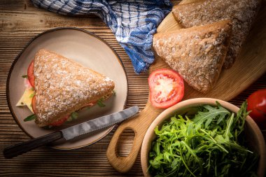 Tahta bir masada peynirli, jambonlu ve domatesli üçlü sandviç..
