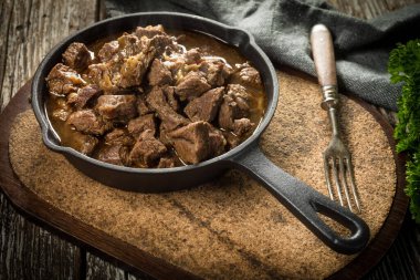 Dökme demir tavada sığır güveci, ahşap arka plan. Sığ alan derinliği.