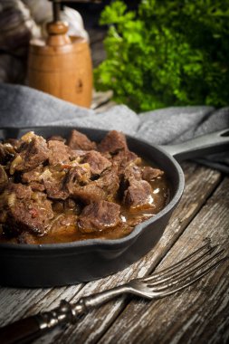 Dökme demir tavada sığır güveci, ahşap arka plan. Sığ alan derinliği.