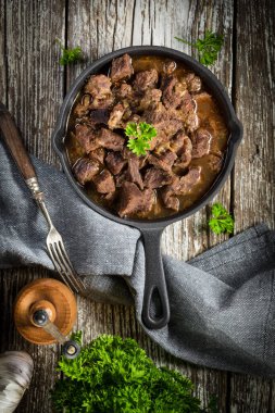Dökme demir tavada sığır güveci, ahşap arka plan. Yüzeyin derinliği. Üst görünüm.