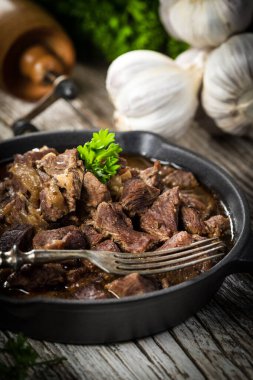 Dökme demir tavada sığır güveci, ahşap arka plan. Sığ alan derinliği.