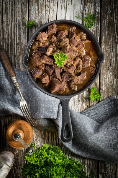 Dökme demir tavada sığır güveci, ahşap arka plan. Yüzeyin derinliği. Üst görünüm.