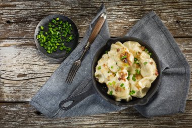 Fırında hamur köftesi (pierogi), içinde dökme demir tavada yeşillikler serpiştirilmiş..