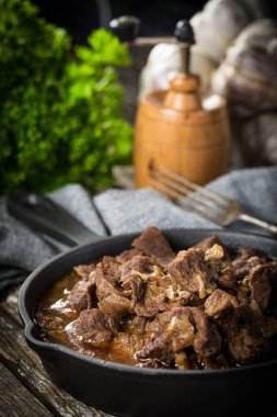 Dökme demir tavada sığır güveci, ahşap arka plan. Sığ alan derinliği.