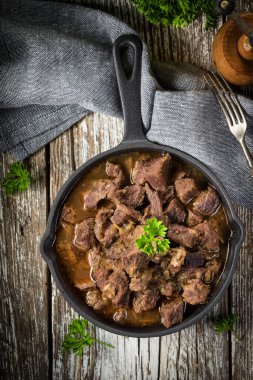 Dökme demir tavada sığır güveci, ahşap arka plan. Yüzeyin derinliği. Üst görünüm.