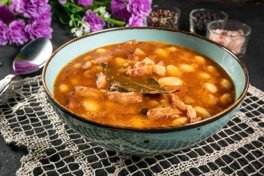 Domates soslu fasulye, pastırma ve siyah kasede sosis. Seçici odak.