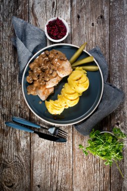 Mantar soslu ızgara tavuk göğsü, patates püresi ve salatalık turşusu ile servis edilir..