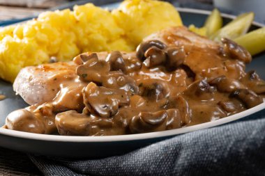 Mantar soslu ızgara tavuk göğsü, patates püresi ve salatalık turşusu ile servis edilir..