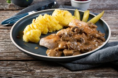 Mantar soslu ızgara tavuk göğsü, patates püresi ve salatalık turşusu ile servis edilir..