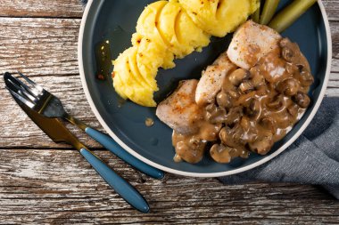 Mantar soslu ızgara tavuk göğsü, patates püresi ve salatalık turşusu ile servis edilir..