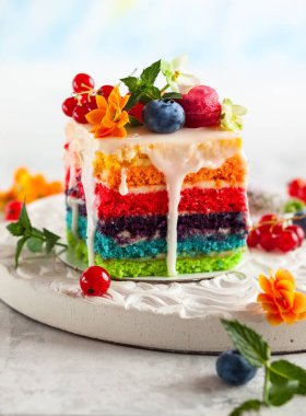Gökkuşağı kek bir dilim taze meyveler ve çiçekler ile tatil için dekore edilmiş