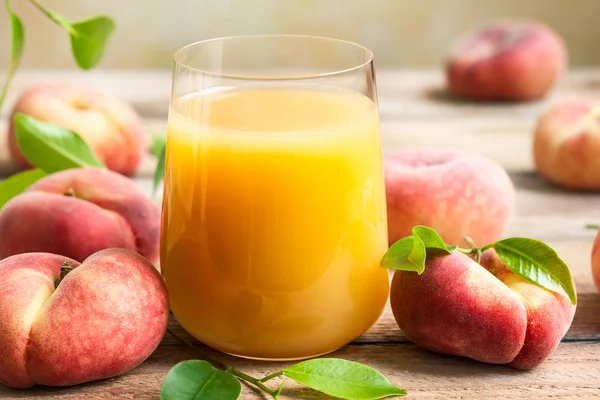 木製のテーブルの上の葉の新鮮なフルーツに囲まれた新鮮な桃ジュースのガラス 健康的な朝食の概念 — ストック写真