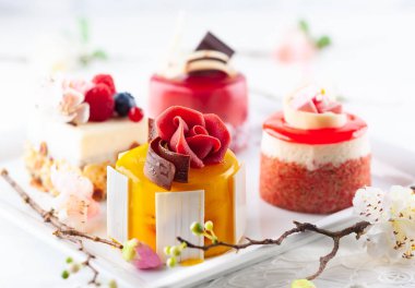 Beyaz tabakta çeşitli mini kekler. Tatil için taze böğürtlen ve çiçeklerle süslenmiş şekerler..