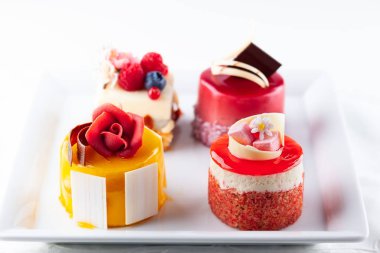 Beyaz tabakta çeşitli mini kekler. Tatil için taze böğürtlen ve çiçeklerle süslenmiş şekerler..