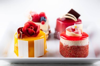 Beyaz tabakta çeşitli mini kekler. Tatil için taze böğürtlen ve çiçeklerle süslenmiş şekerler..