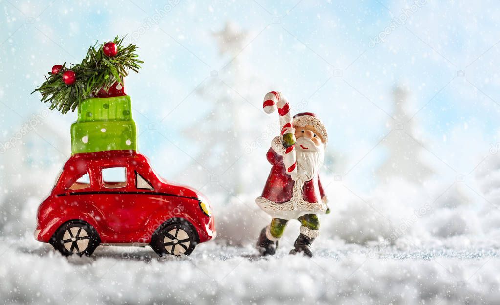 Santa Claus and red toy car carrying Christmas gifts in snowy landscape. Christmas concept with copy space.