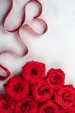 Kırmızı gül ve kırmızı kurdele vintage beyaz-gri arka plan üzerinde kalp şeklinde. Sevgililer günü için festival kavram. Kopya alanı ile üstten görünüm.