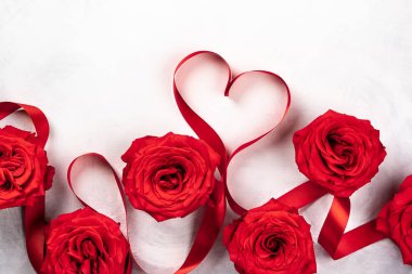 Kırmızı gül ve kırmızı kurdele vintage beyaz-gri arka plan üzerinde kalp şeklinde. Sevgililer günü için festival kavram. Kopya alanı ile üstten görünüm.