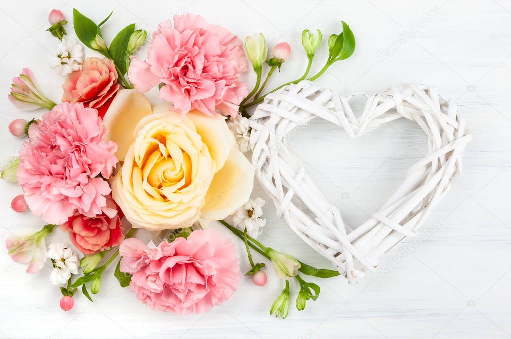 Beautiful spring flowers on white wooden background. Festive floral composition with heart from wooden branches. Valentine's day or mother's day concept. Top view.