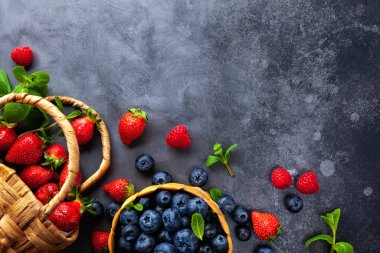 Taze organik yaban mersini, ahududu ve çilek. Mini sepetli nane yaprağı ve klasik siyah masa. Sağlıklı beslenme kavramı. Üst görünüm, alanı kopyala.