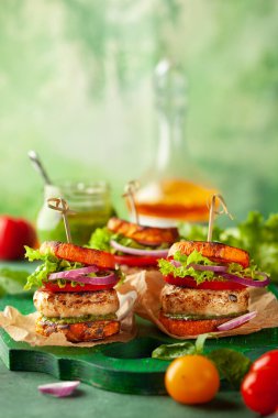 Lezzetli kavrulmuş balkabaklı hindi burger, domatesli ve ahşap panoda pesto..