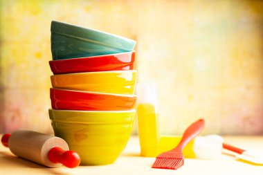 Mutfak aletleri arka planda seramik çok renkli kaseler, merdane, sarı arka planda spatula. Ev mutfağı dekorasyonu kavramı. Ön görünüm, boşluğu kopyala.