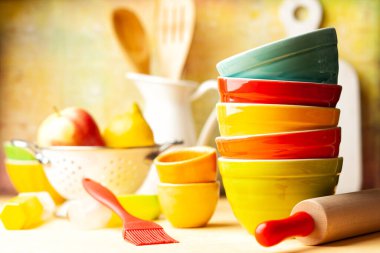 Mutfak aletleri ve seramik çok renkli çanaklar, merdane, sürahi, süzgeç, sarı arka planda spatula. Ev mutfağı dekorasyonu kavramı.