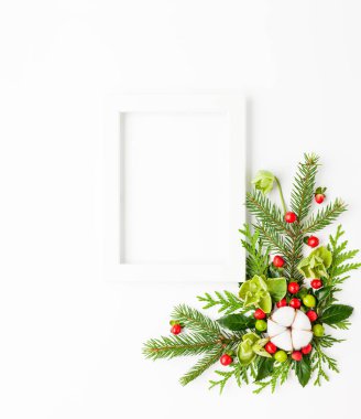 Fotoğraf çerçeveli Noel kompozisyonu, pamuk çiçeği, ladin dalları ve beyaz arka planda kırmızı böğürtlenli çoban püskülü. Tatil mesajları için boş yeri olan mutlu noel tebrik kartları. Düz yatıyordu