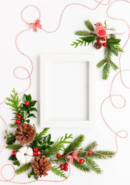 Fotoğraf çerçeveli Noel kompozisyonu, pamuk çiçeği, ladin dalları ve beyaz arka planda kırmızı böğürtlenli çoban püskülü. Tatil mesajları için boş yeri olan mutlu noel tebrik kartları. Düz yatıyordu
