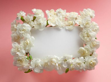 Pastel pembe arka planda beyaz karanfillerden yapılmış şenlik çiçekleri çerçevesi ve boş tebrik kartı. Düz yatış, üst görünüm.