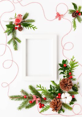 Fotoğraf çerçeveli Noel kompozisyonu, pamuk çiçeği, ladin dalları ve beyaz arka planda kırmızı böğürtlenli çoban püskülü. Tatil mesajları için boş yeri olan mutlu noel tebrik kartları. Düz yatıyordu