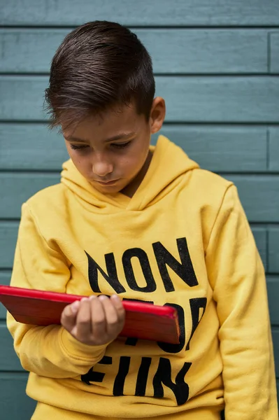 Boy with yellow sweatshirt surfing with his tablet . Wooden green Background