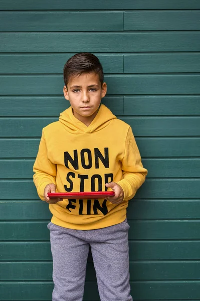 Niño con sudadera amarilla surfeando con su tableta. Fondo verde madera —  Fotos de Stock