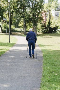 Parkta bastonla yürüyen yaşlı adam