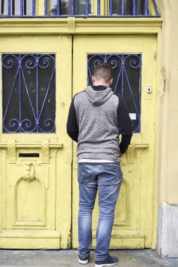 Genç bir adam evine giriyor. Sarı ahşap kapı.