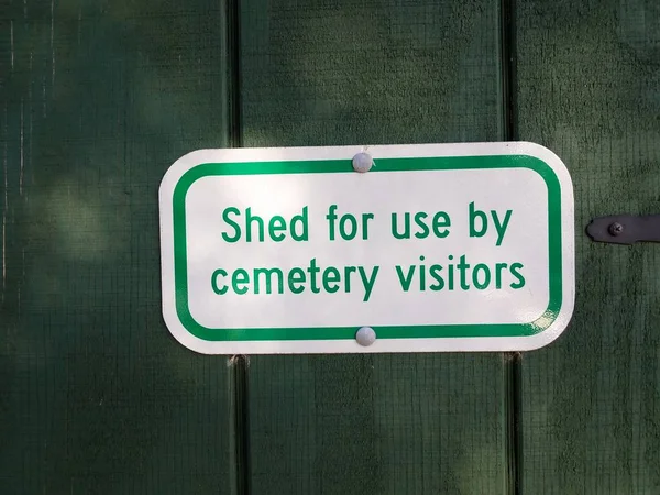 Shed for use by cemetery visitors sign on green wood — Stock Photo, Image