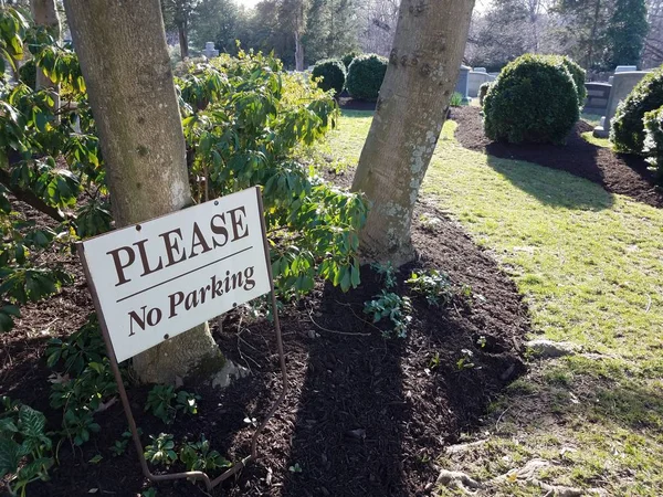 Blanco por favor no hay señal de aparcamiento y hojas verdes y plantas en el cementerio — Foto de Stock