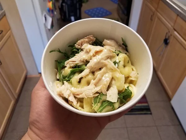 Mano sosteniendo arco de pollo y pasta y verduras en la cocina —  Fotos de Stock