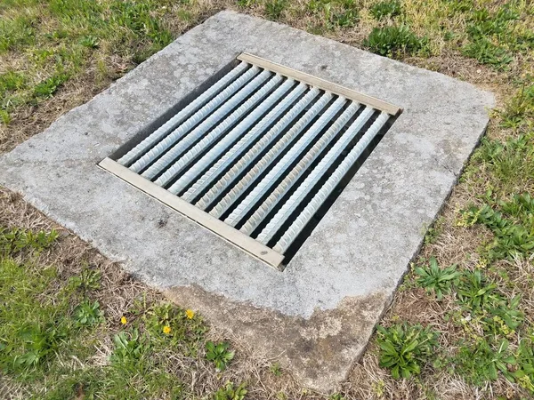 Cement and metal grate or bars with drain and green grass — Stock Photo, Image
