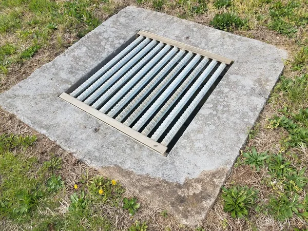 Cement and metal grate or bars with drain and green grass — Stock Photo, Image