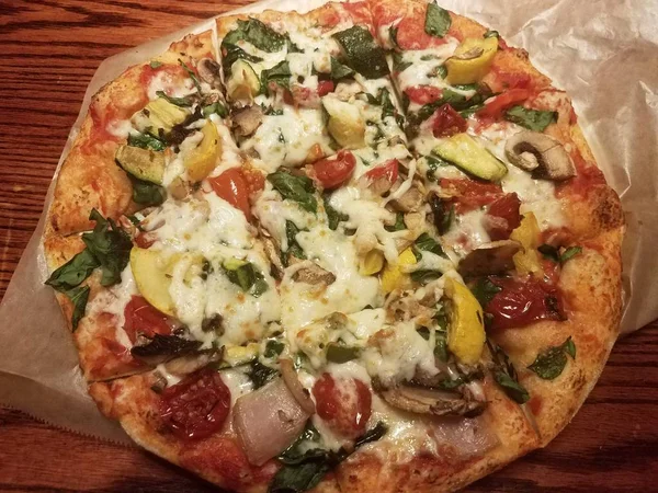 vegetable pizza with cheese and wax paper on table