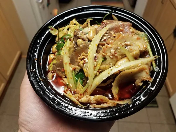 Mão segurando tigela de carne chinesa e fatias de intestino em óleo picante na cozinha — Fotografia de Stock